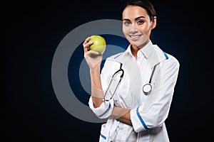 Young smiling lady doctor holding apple and looking camera isolated