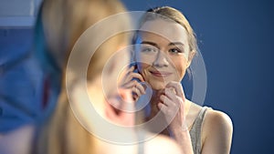 Young smiling lady looking at mirror reflection, happy with skin treatment