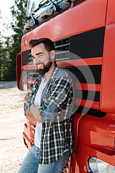 Young smiling male truck driver beside his red cargo truck