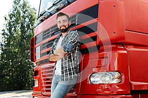 Young smiling male truck driver beside his red cargo truck