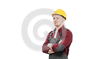 Young smiling male worker in a construction worker, in a yellow helmet, working overalls and a red checkered shirt on a