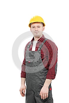 Young smiling male worker in a construction worker, in a yellow helmet, working overalls and a red checkered shirt on a