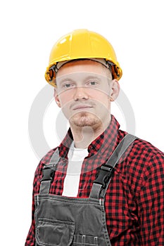 Young smiling male worker in a construction worker, in a yellow helmet, working overalls and a red checkered shirt on a