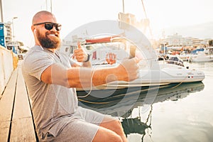 Young smiling man with beard is making selfie or video broadcast with smartphone on stabilizer or stabiliser and showing thumb up