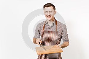 Young smiling man chef or waiter in striped brown apron, shirt holding wooden cutting board, knife isolated on white