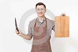 Young smiling man chef or waiter in striped brown apron, shirt holding wooden cutting board, knife isolated on white