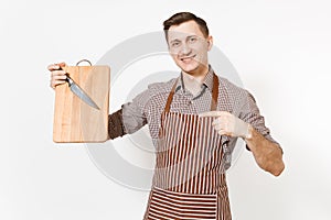 Young smiling man chef or waiter in striped brown apron, shirt holding wooden cutting board, knife isolated on white