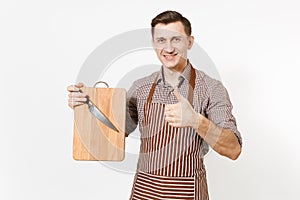 Young smiling man chef or waiter in striped brown apron, shirt holding wooden cutting board, knife isolated on white