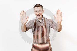 Young smiling man chef or waiter in striped brown apron, shirt showing palms to camera isolated on white background