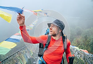 Young smiling man crossing canyon over Suspension Bridge and touching multicolored Tibetan Prayer flags hinged over gorge. Mera