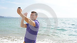 Young smiling man having a video call on smart phone at the sea beach. Happy guy making video online chats on beautiful