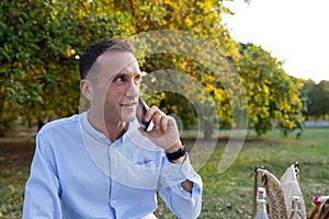 Young smiling man in his thirties while picnicking in the park makes a phone call