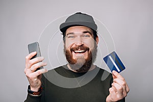 Young smiling man holding a card and a phone. Shopping and paying online.