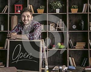 Young smiling man leather worker standing near open sign at table with tools