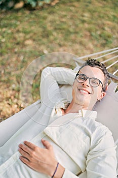 Young smiling man lies in a hammock in the garden with his hand under his head