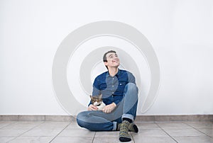 Young smiling man looking up sitting on the floor of new house with his cat.