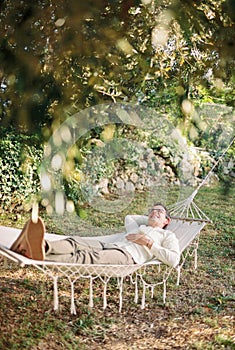 Young smiling man lying in a hammock in a green garden