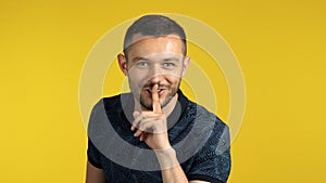 Young smiling man making hush gesture, keeps finger on lips