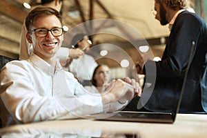 Young smiling man in official clothes and glasses, working on laptop at stylish modern office.