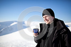 Young smiling man photographer in winter clothing drinking tea from thermos