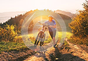 Young smiling man pushing a mountain bike up the hill. Active adventure travel on bicycle