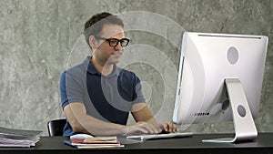 Young smiling man sitting at his desk in the office and working on the computer.