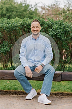 Young smiling man is sitting on a park bench. The concept of rest and relaxation