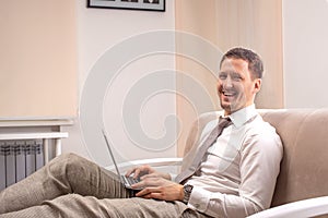 A young  smiling man sitting on sofa and working on his laptop