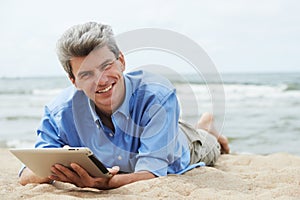 Young smiling man with tablet pc on seashore