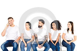 young smiling man talking on smartphone while multiethnic group of young people sitting on chairs isolated