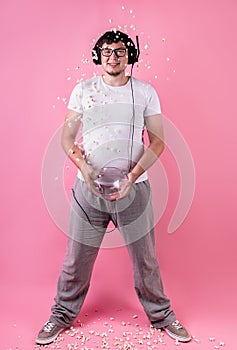 Young smiling man throwing popcorn into the air isolated on pink