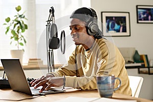 Young smiling man typing on laptop keyboard and speaking in microphone