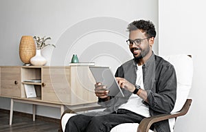 Young smiling man using digital tablet computer at home, Leisure, relaxation, online learning, web chat concepts