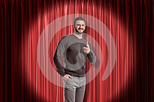 Young smiling man wearing casual clothes and pointing finger on red stage curtains background