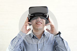 Young smiling man wearing tshirt and virtual reality headset or VR glasses, playing video game, white background
