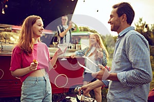 Young smiling man and woman cooking meat, doing barbecue, drinking cocktails and talking. Blurred people on background