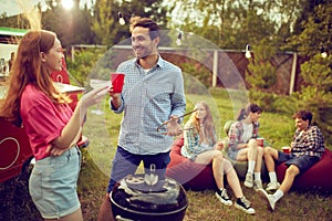 Young smiling man and woman doing barbecue, drinking cocktails and talking. Blurred people on background. Good time