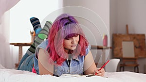 Young smiling middle aged woman writing in the book. Drawing. Plus size girl is lying in bed. Relaxing days.