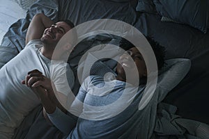 Young smiling mixed race couple lying together in bed