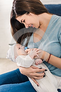 Young smiling mother with little baby with pacifier sitting on bed