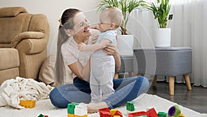 Young smiling mother playing with her baby son in toy cars at home. Concept of family having time together and children