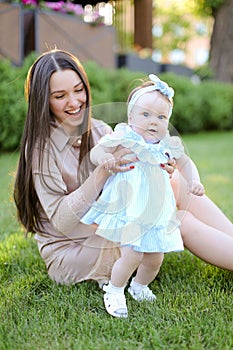 Young smiling mother sitting on grass with little daughter.