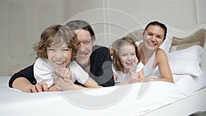 Young Smiling Parents with Two Children are Having Fun Together in Their Bedroom. Joyous Family on White Bed.