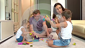 Young smiling parents and two little children playing board game at home