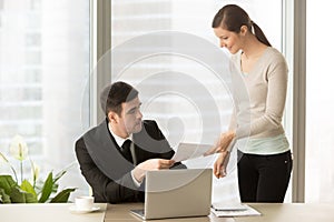 Young smiling personal assistant giving document to boss, paperw