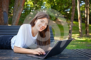 Young smiling pretty student woman, lying on the bench in park