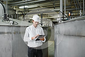 Young smiling professional in overalls and protective helmet standing in front of camera inside large machinebuilding plant