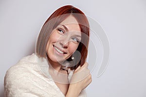 Young smiling red haired girl in knitted beige sweater on white background looking sideways. Concept photo shoot in studio
