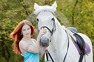 Young smiling red-haired woman holds white horse