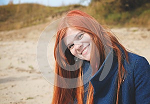 young smiling red haired woman wearing a blue coat and looking at viewer. autumn portrait of happy ginger hair woman.